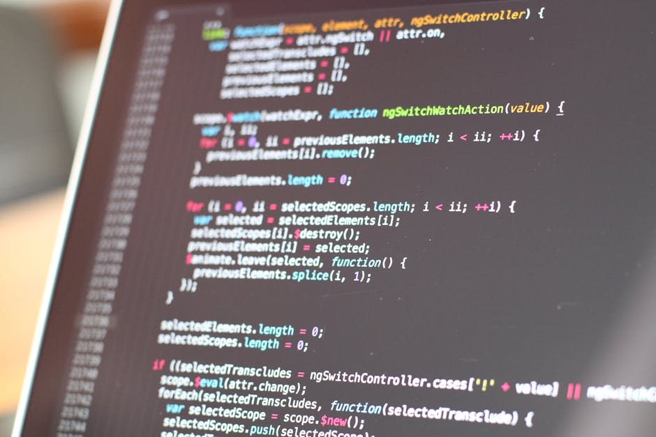 Photograph of a computer screen displaying a blurred and colorful array of programming code, with various lines of text in different colors including red, green, blue, yellow, and white. The code appe